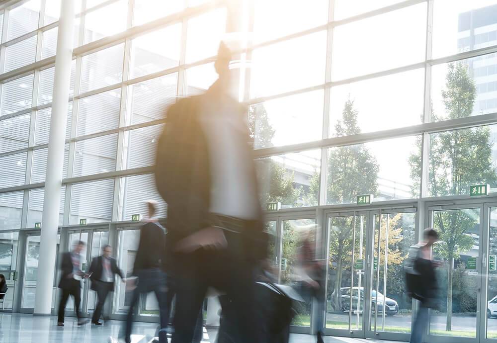Menschen in Bewegung in heller Glaslobby – Karriere, Entwicklung und Chancen bei IPConcept.