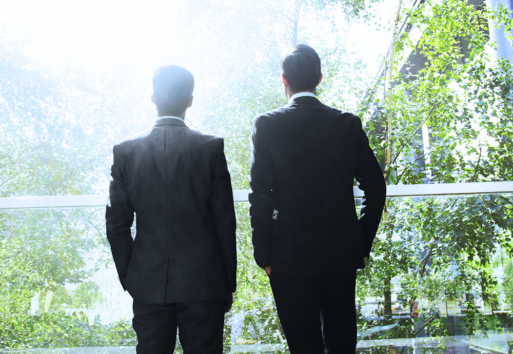 Zwei Geschäftsleute im Anzug blicken ins Grüne – Verantwortung und Nachhaltigkeit bei IPConcept.