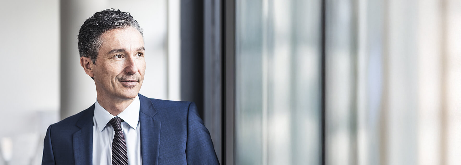 Geschäftsmann blickt zuversichtlich aus dem Fenster – Partnerschaft und Wachstum durch professionellen Vertriebsservice.