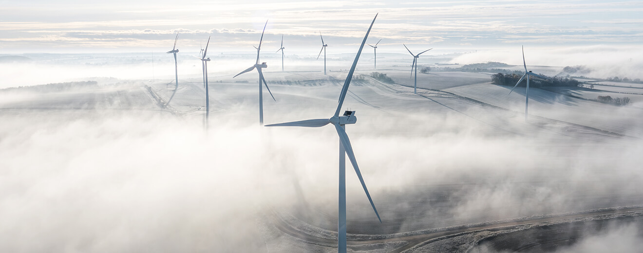 Windräder im Nebel über Feldern – Symbol für Nachhaltigkeit und erneuerbare Energien bei IPConcept.